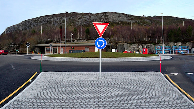 Fotografi av en rundkjøring sett rett forfra, med grøntareal i senterøya og kjørebane rundt. Bildet brukes som eksempel på sideposisjon R0 i senter av rundkjøringen og H langs ytterkanten.